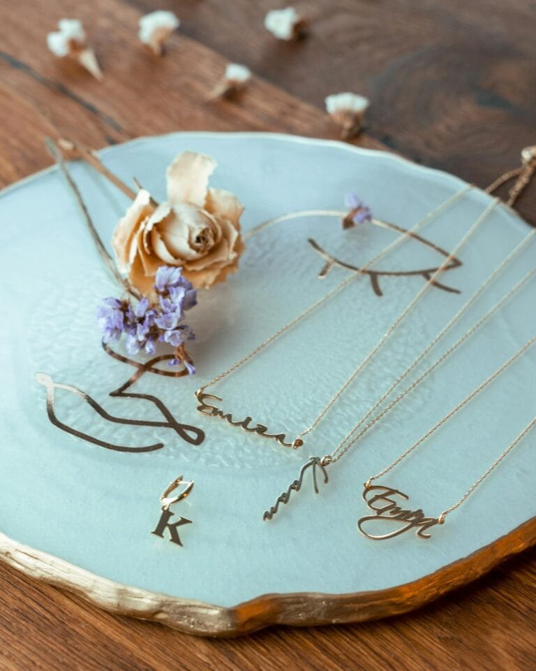 Artistic shot of gold necklaces with floral decor on a ceramic plate.